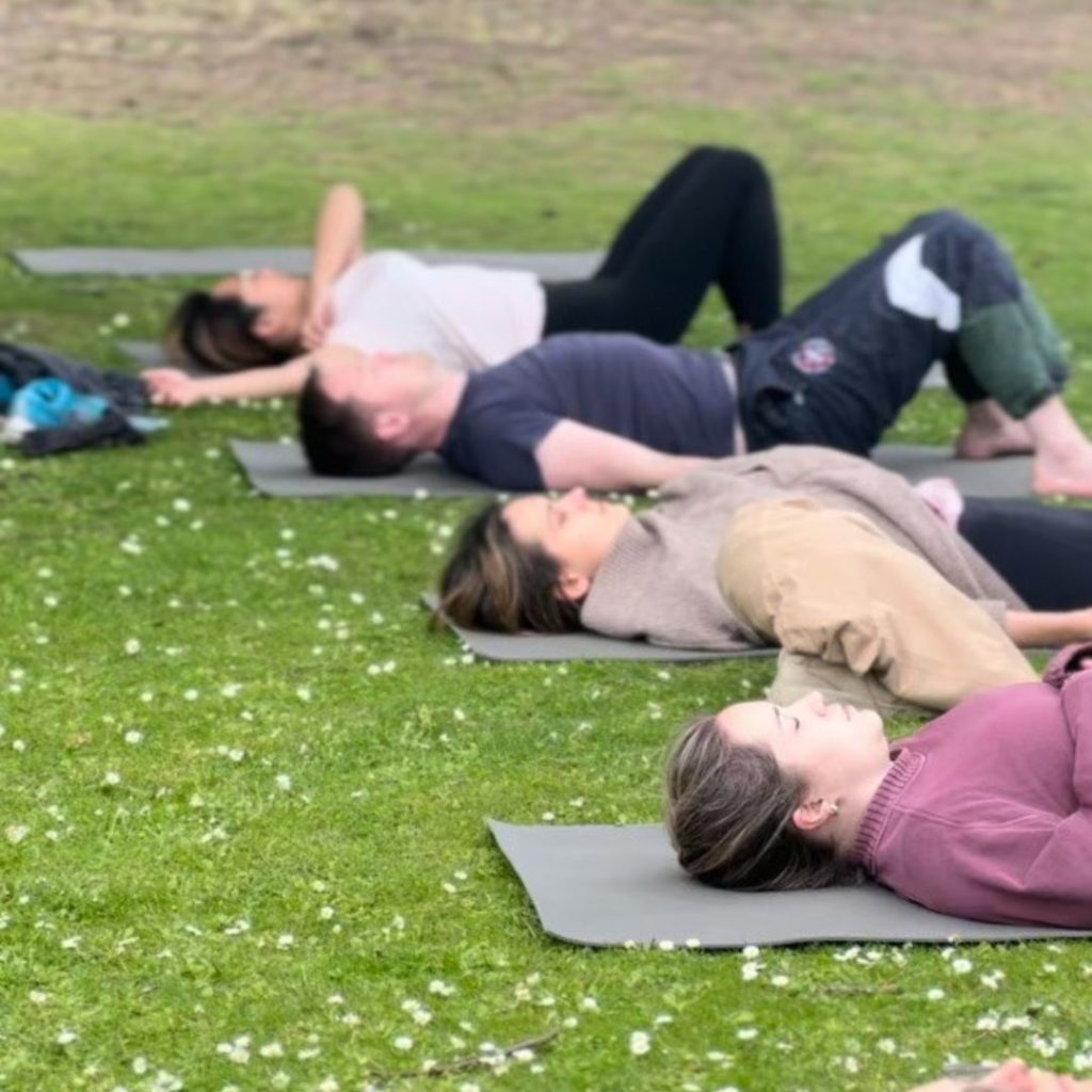 People lying on their backs on yoga mats on grass